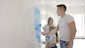 Young family paints wall with a roller while mother checking a text message