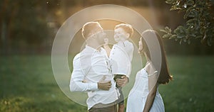 Young family: parents playing with their toddler son. Happy mother and father hugging their baby, smiling outdoors on a