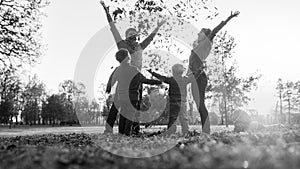 Young family playing with autumn leaves in a monochrome greyscale image