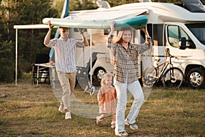 a young family is playing next to their mobile home. Dad and mom are carrying a sup board and daughter is walking next