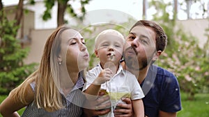 Young family playing in the park. Father, mother and baby happy boy sat down together near the flower. Blonde boy