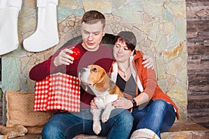 Young family playing with pretty beagle dog near fireplace