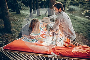 Young family playing with son on a hammock in park on camping trip, hipster mother smiling at baby boy near handsome father