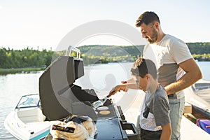 Young family preparing hamburger on a grill outdoors close to a lake