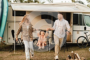 a young family is resting near their mobile home. Dad, mom and daughter play near the motorhome