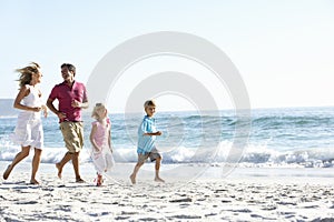 Young Family Running Along Sandy Beach On Holiday