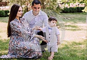 Young family sits on a green lawn, dad, mom and little son