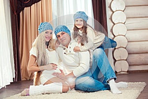 Young family sitting on floor. in a winter sweater and hat, the concept of Christmas. pregnancy in a wooden house