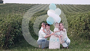 Young family sitting in the green field with two sons