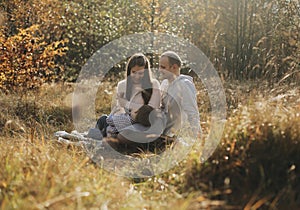 Young family sitting In long grass in autumn forest