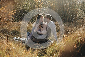 Young family sitting In long grass in autumn forest