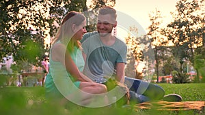 Young family is sitting on rug in park in summer, parents kiss, relax concept