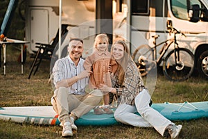 a young family is sitting on a sup board next to their mobile home