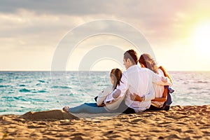 Young family sitting together in late afternoon sun on beach