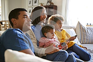 Young family sitting together on the sofa in their living room watching TV, selective focus