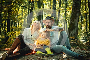 A young family with small child having picnic in autumn nature at sunset. Happy family of three lying in the grass in
