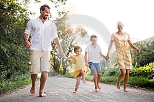 A young family with small children playing hopscotch on a road in summer.