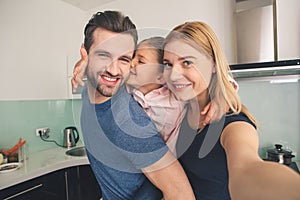 Young family smiling taking pictures together in kitchen