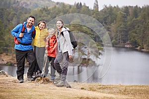 Young family standing on a rock by a lake looking to camera embracing, full length