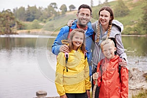 Young family standing on the shore of a lake in the countryside looking to camera smiling, Lake District, UK