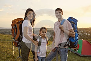 Young family of three with backpacks at campsite in mountains. Happy parents and daughter enjoying summer hiking trip