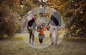 Young family of three with pregnant beautiful mother, daughter and father spending time together at the autumn park. Copy space