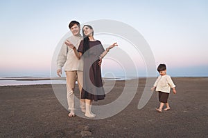 Young family with a three year old son walks barefoot along the wild evening beach. Family look linen clothes