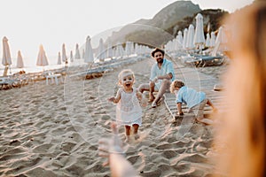 Young family with toddler children having fun on beach on summer holiday.