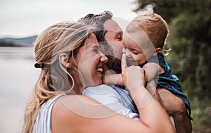 A young family with a toddler girl outdoors by the river in summer.