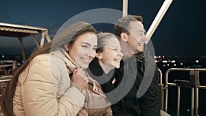 Young family together on the Ferris wheel. In the evening in the amusement park the father, mother and daughter on merry