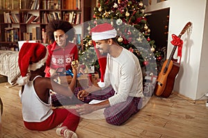 Young family together with little girl child celebrating Christmas and opening present..