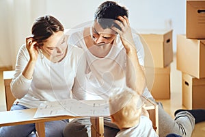 Family together at living room of new apartment assembling furniture, pile of moving boxes on background