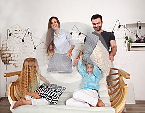 Young family and two children play at home fighting with pillows