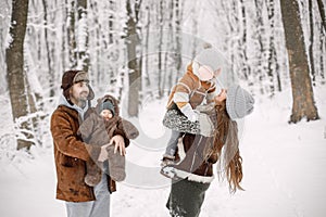 Young family with two children standing in winter forest and posing for a photo