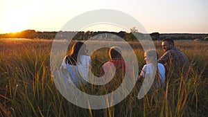Young family with two kids spending time together at meadow. Mommy and daddy with small children sitting on grass at
