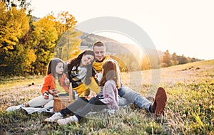 A young family with two small children having picnic in autumn nature at sunset.