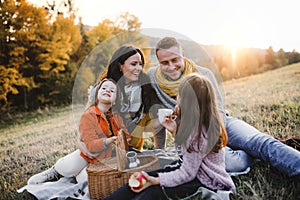 A young family with two small children having picnic in autumn nature at sunset.