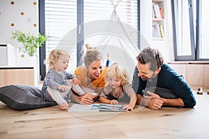 Young family with two small children indoors in bedroom reading a book.