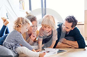 Young family with two small children indoors in bedroom reading a book.