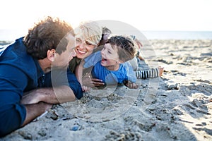 Young family with two small children lying down outdoors on beach.