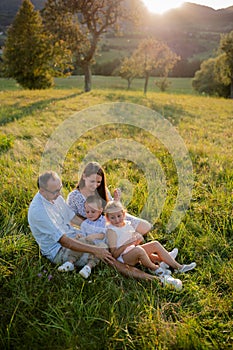 Young family with two small children sitting on meadow outdoors at sunset.