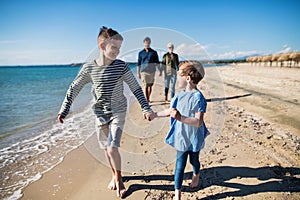 Young family with two small children walking outdoors on beach.