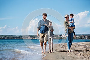 Young family with two small children walking outdoors on beach.