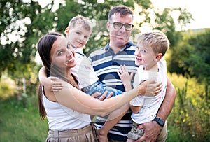 A young family with two small sons standing outdoors in nature on a summer day.