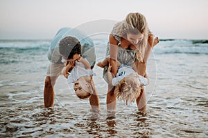 A young family with two toddler children having fun on beach on summer holiday.