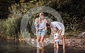 Young family with two toddler children outdoors by the river in summer, playing.