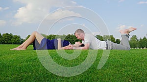 A young family is waiting for a child. A man kisses his pregnant wife, together lie on the grass in the park