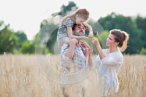 Young family walking through a field of corn on a summers day the father is carrying his younger daughter on his shoulders