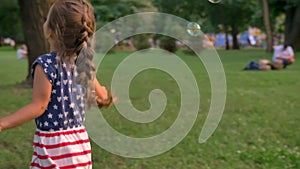 Young family is walking in park in summer, daughter runs and catches bubbles, childhood concept