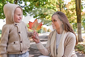 Young family, woman mom holds autumn leaf, little boy son smiling happy looking. Emotions joy, smile and relaxation